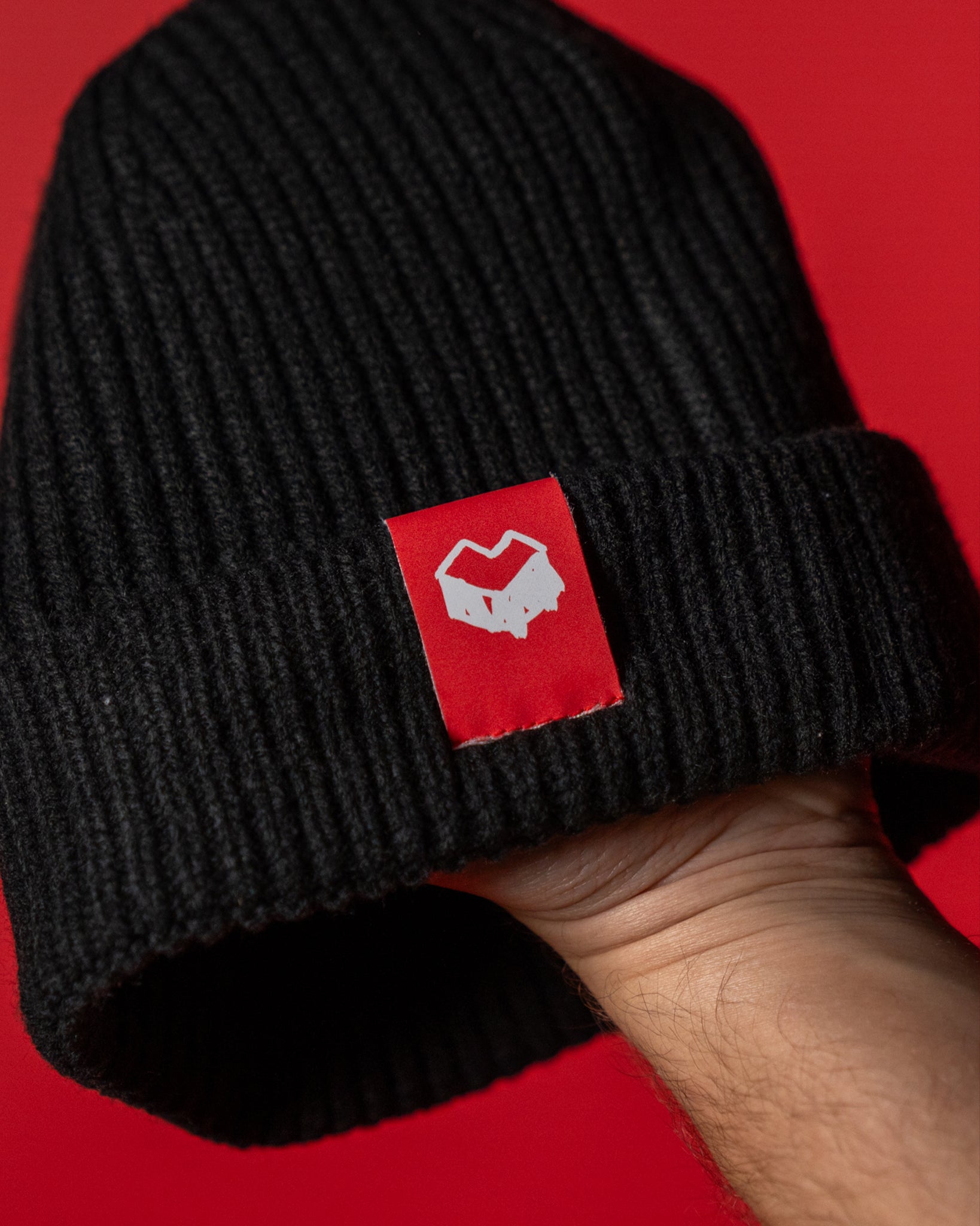 Schwarze Beanie aus grobem Rippstrick mit breiter Umschlagkante. Auf der Vorderseite ist ein rotes Label mit dem weißen „Loot für die Welt“-Logo angebracht. Die Mütze besteht aus weichem, wärmendem Material und bietet einen lässigen, modernen Look für Alltag und Streetwear-Stil.