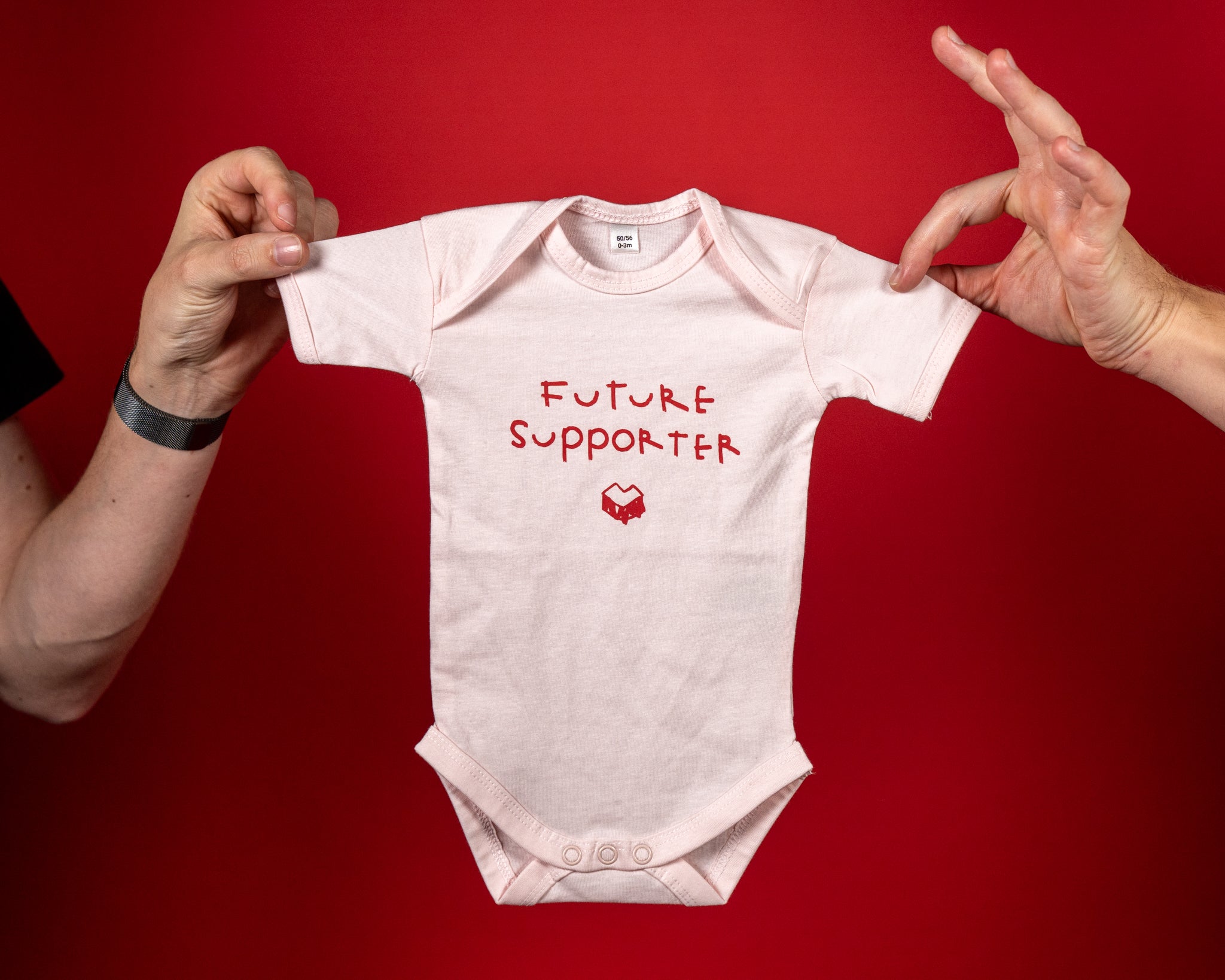 Hellrosa Babybody aus weicher Baumwolle mit kurzen Ärmeln und Rundhalsausschnitt. Auf der Vorderseite steht in roter, handschriftlicher Schrift der Text „FUTURE SUPPORTER“, darunter das rote „Loot für die Welt“-Logo. Der Body verfügt über praktische Druckknöpfe im Schrittbereich und bietet dank seines elastischen Materials hohen Tragekomfort für Babys.