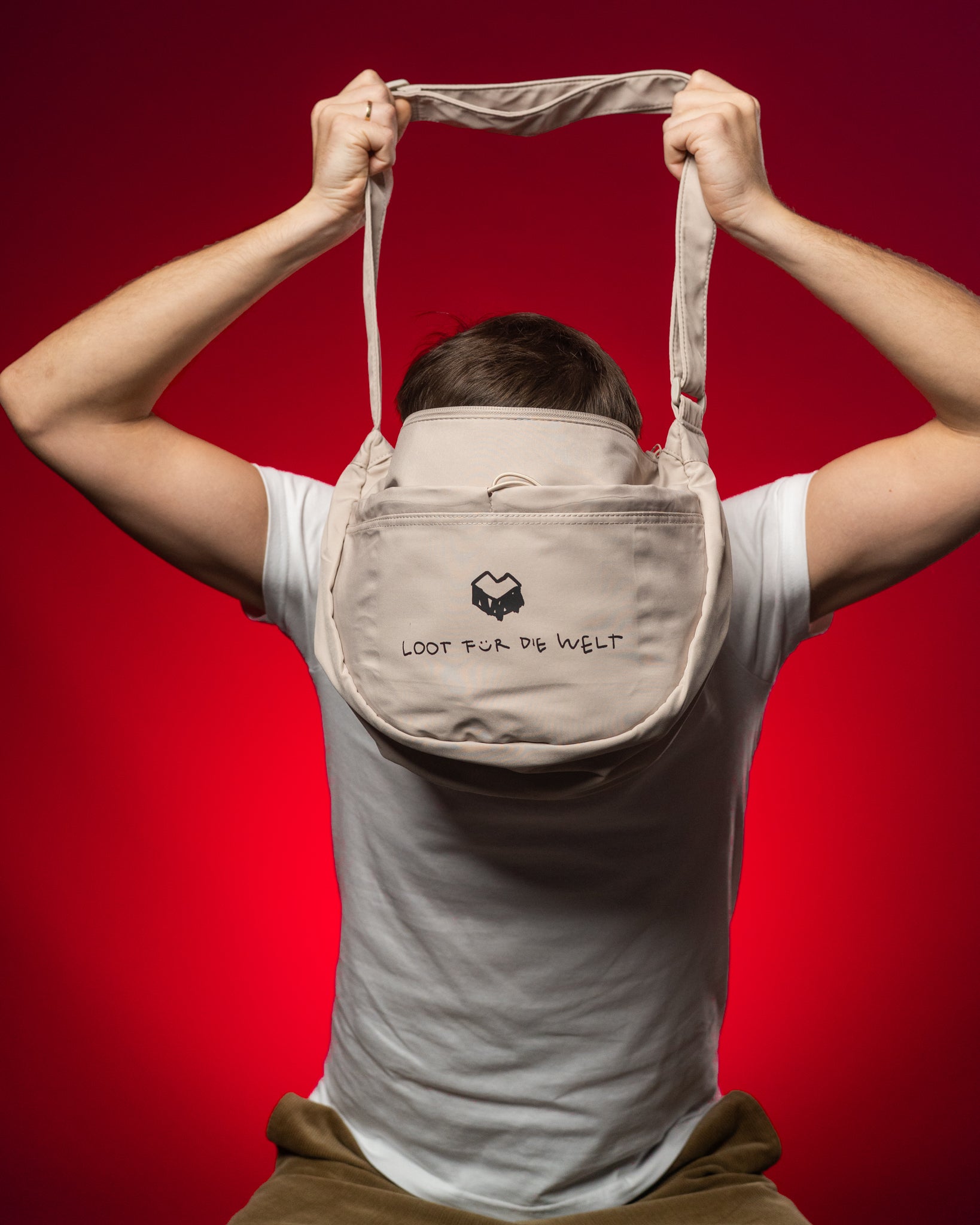 Offwhite-farbene Umhängetasche mit schwarzem Logo und dem Schriftzug „LOOT FÜR DIE WELT“ auf der Vorderseite. Die Tasche besteht aus glattem, strapazierfähigem Material und hat einen verstellbaren Schultergurt. Sie wird hier hochgehalten, wodurch ihre runde Form und das großzügige Hauptfach gut sichtbar sind. Das minimalistische Design vereint Funktionalität und modernen Streetwear-Stil.