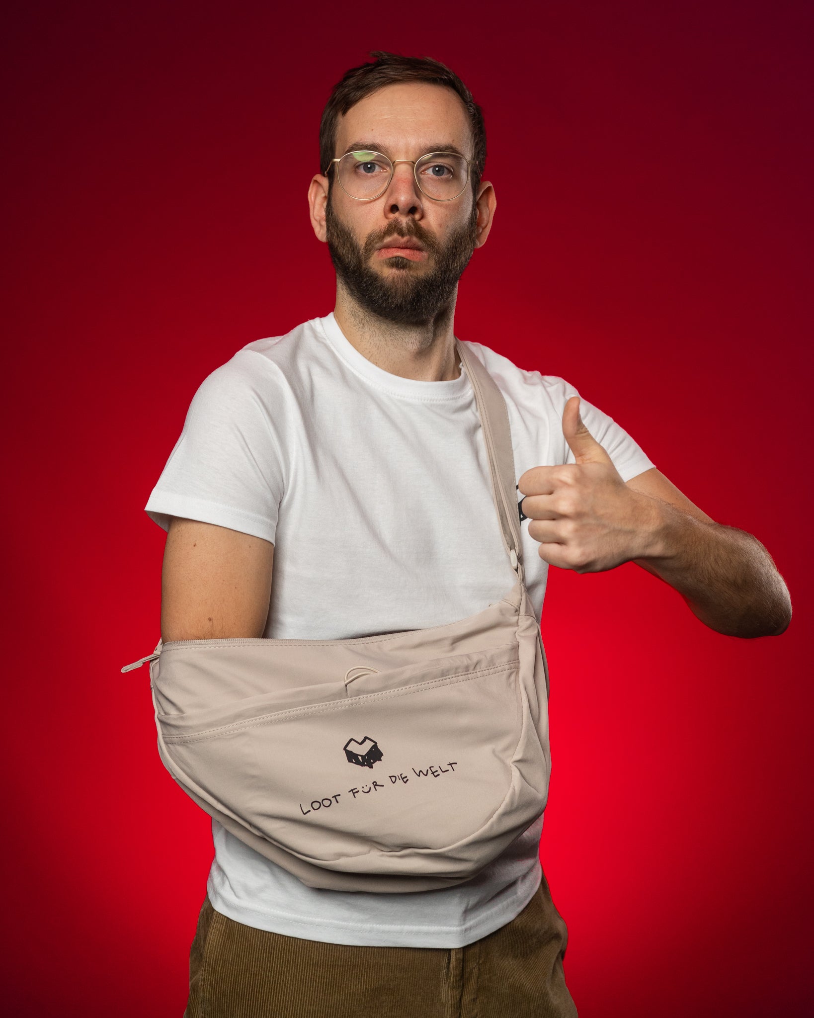 Offwhite-farbene Umhängetasche mit schwarzem Logo und dem Schriftzug „LOOT FÜR DIE WELT“ auf der Vorderseite. Die Tasche besteht aus glattem, leicht strukturiertem Stoff und verfügt über einen verstellbaren Schultergurt. Das geräumige Hauptfach wird mit einem Reißverschluss geschlossen. Das Design ist schlicht und modern – ideal für Alltag, Events oder Reisen.