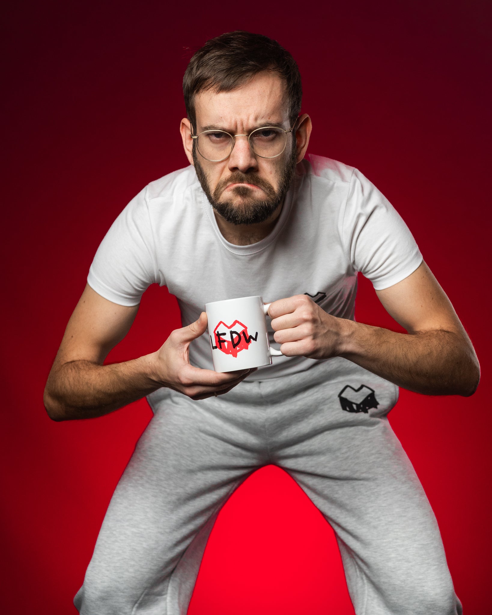 Weiße Keramiktasse mit dem roten Herz-Logo und dem schwarzen Schriftzug „LFDW“ im handschriftlichen Stil. Der Aufdruck steht für „Loot für die Welt“ und kombiniert verspielte Typografie mit einem markanten Symbolmotiv. Der Fokus liegt auf dem klar erkennbaren Tassenmotiv im Zentrum des Bildes.