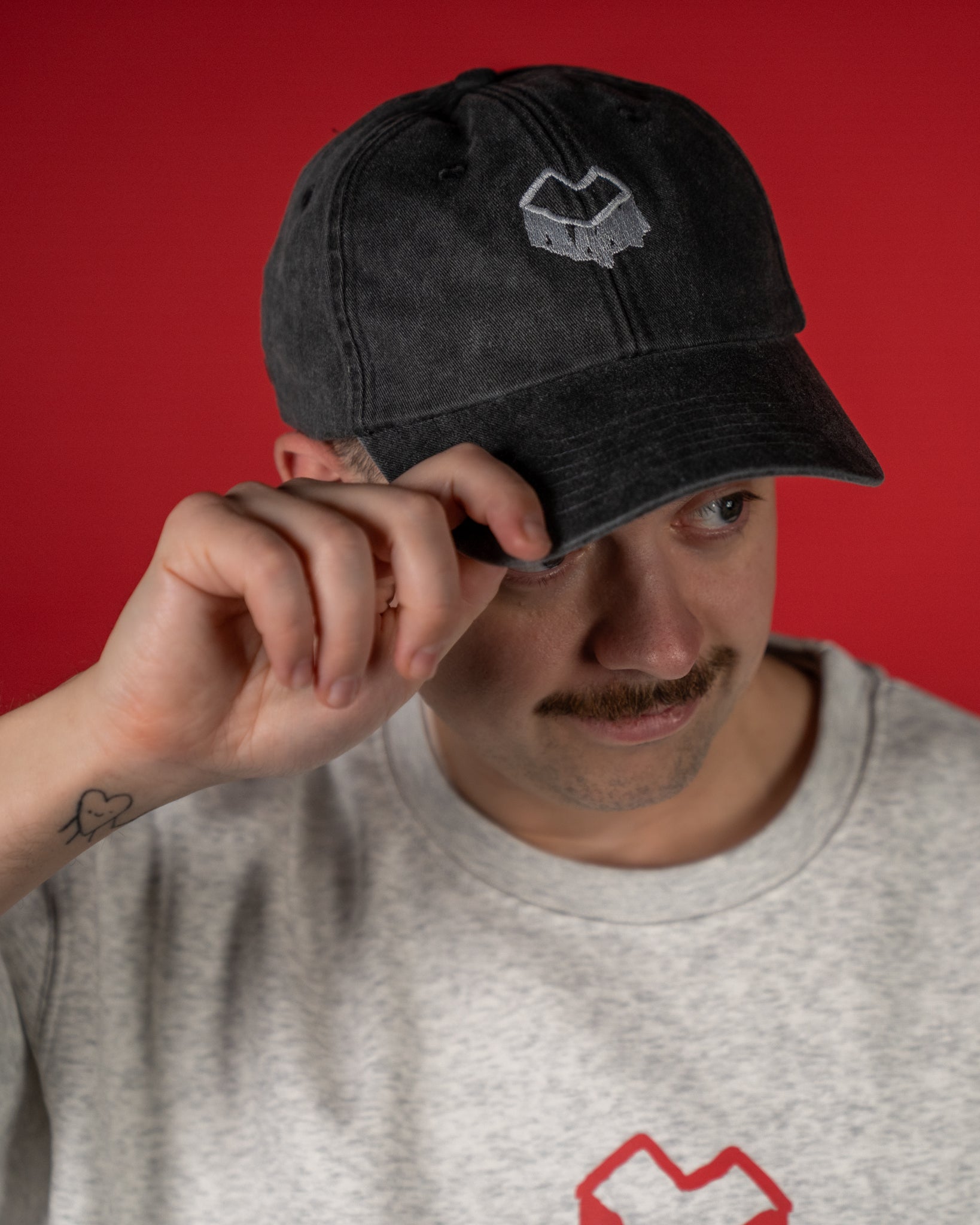 Schwarze Cap aus gewaschener Baumwolle mit leicht gebogener Krempe. Auf der Vorderseite ist ein weißes, geometrisches Herzlogo aufgestickt. Die Cap besitzt eine klassische Sechspanel-Struktur mit Ziernähten und kleinen Belüftungslöchern und wirkt durch den Vintage-Washed-Look lässig und modern.