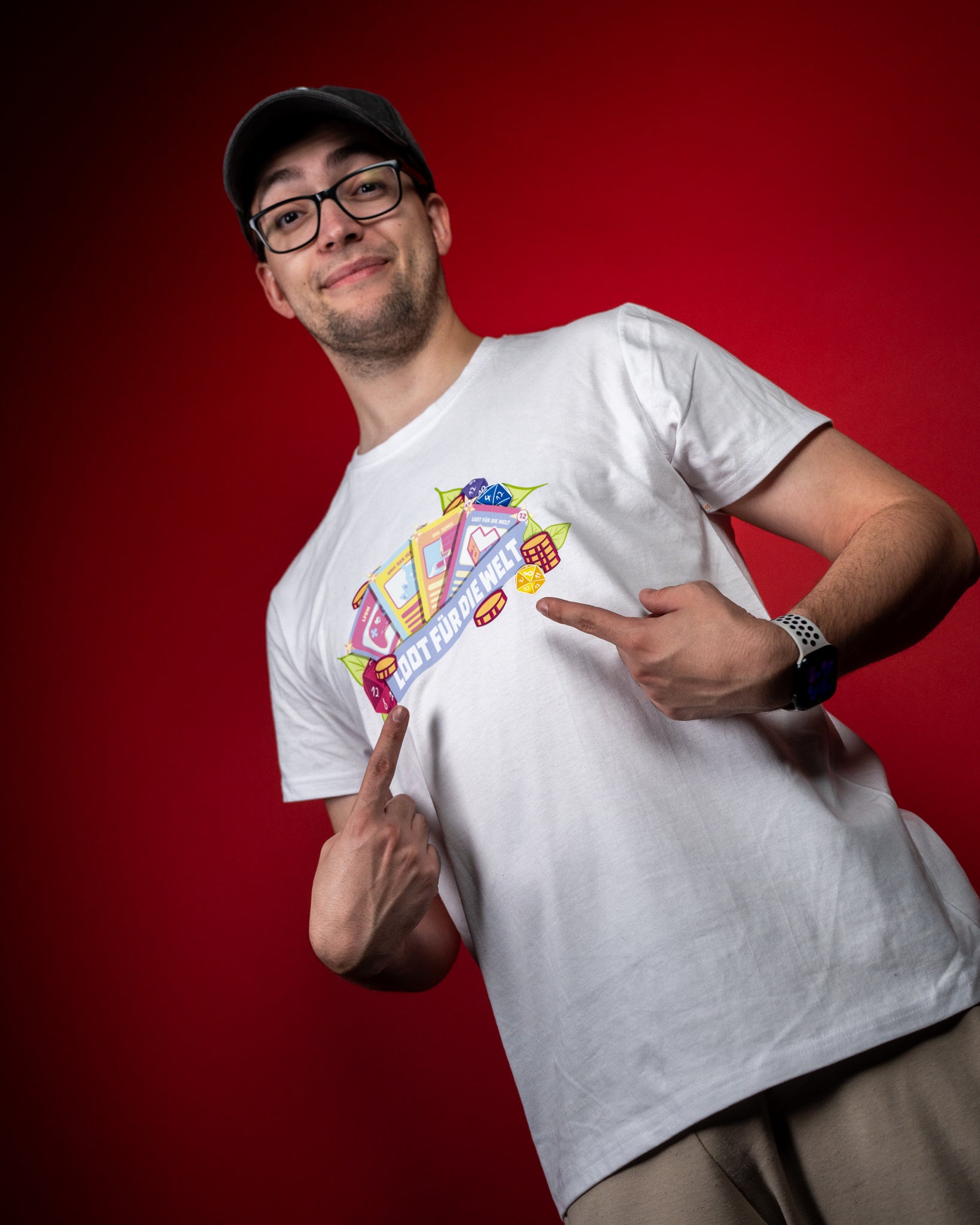 Weißes T-Shirt mit farbenfrohem Frontprint. Das Motiv zeigt eine Sammlung von Spielelementen – darunter Karten, Würfel, Münzen und Symbole – die in einem lebendigen Arrangement gestaltet sind. In der Mitte verläuft ein blaues Banner mit dem Schriftzug „LOOT FÜR DIE WELT“. Das Design wirkt verspielt, detailreich und steht für Gemeinschaft und Spaß am Gaming.