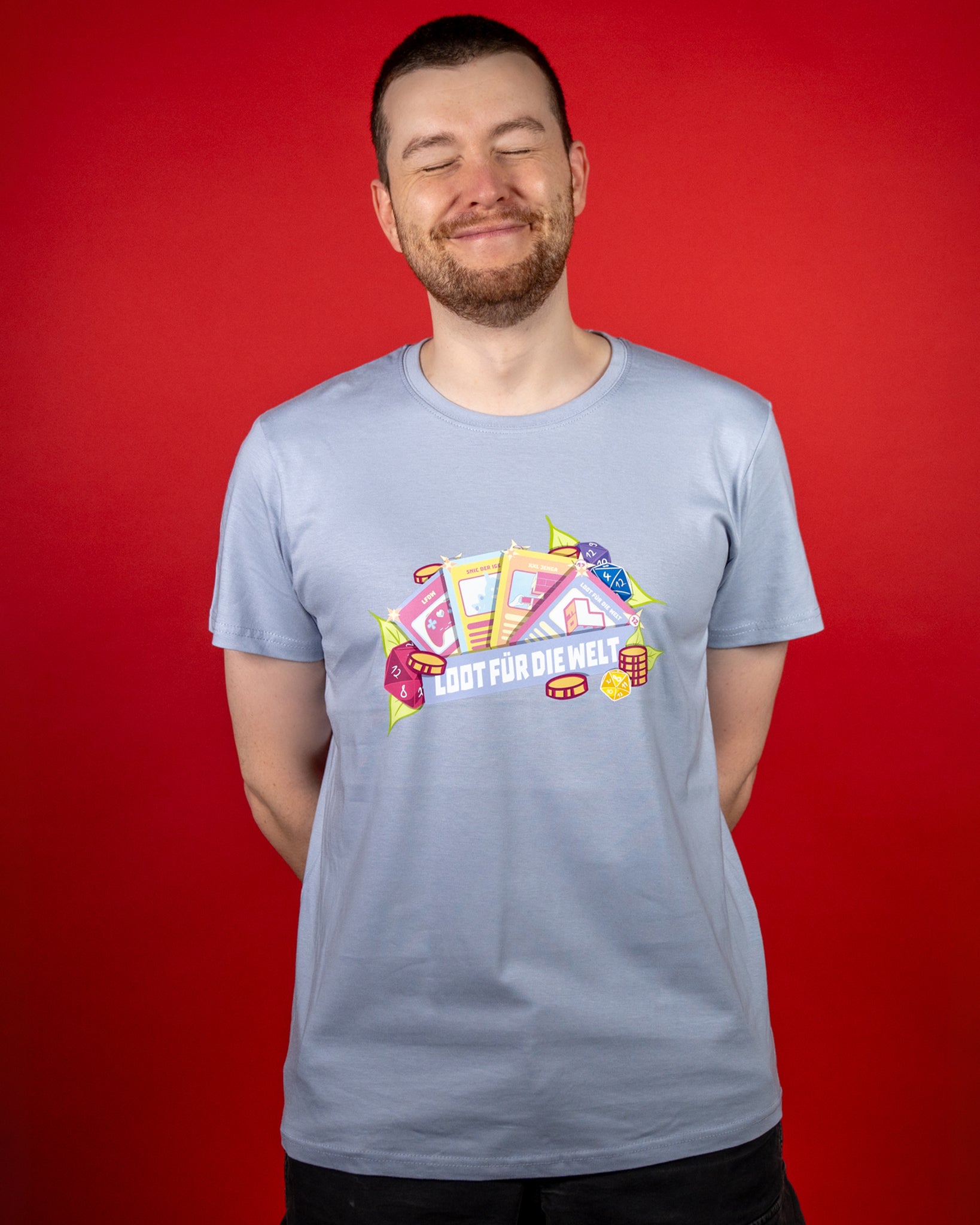 Hellblaues T-Shirt mit großem, detailreichen Frontprint: mehrere Karten mit Gaming-Motiven (Controller, Bauklötze/Jenga, Würfel, Münzen) fächern sich auf. Davor liegt ein Banner mit dem weißen Schriftzug „LOOT FÜR DIE WELT“. Der kontrastreiche Druck steht klar vom hellblauen Stoff ab.
