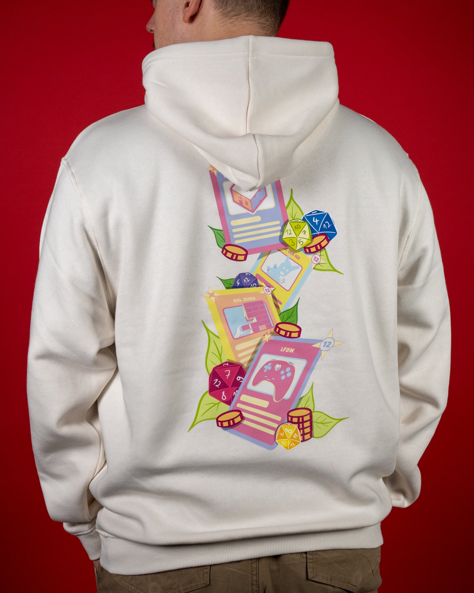 Off-White Hoodie mit großem, buntem Rückendruck. Das Motiv zeigt mehrere Spielkarten, bunte Würfel und Pokerchips, umgeben von grünen Blättern. Auf den Karten sind Symbole wie ein Controller und das „Loot für die Welt“-Logo zu sehen. Der Hoodie besteht aus weichem Baumwollmaterial, hat Rippbündchen an Ärmeln und Saum sowie eine Kapuze mit Kordelzug. Locker geschnittener Unisex-Stil mit auffälligem Gaming-Motiv.