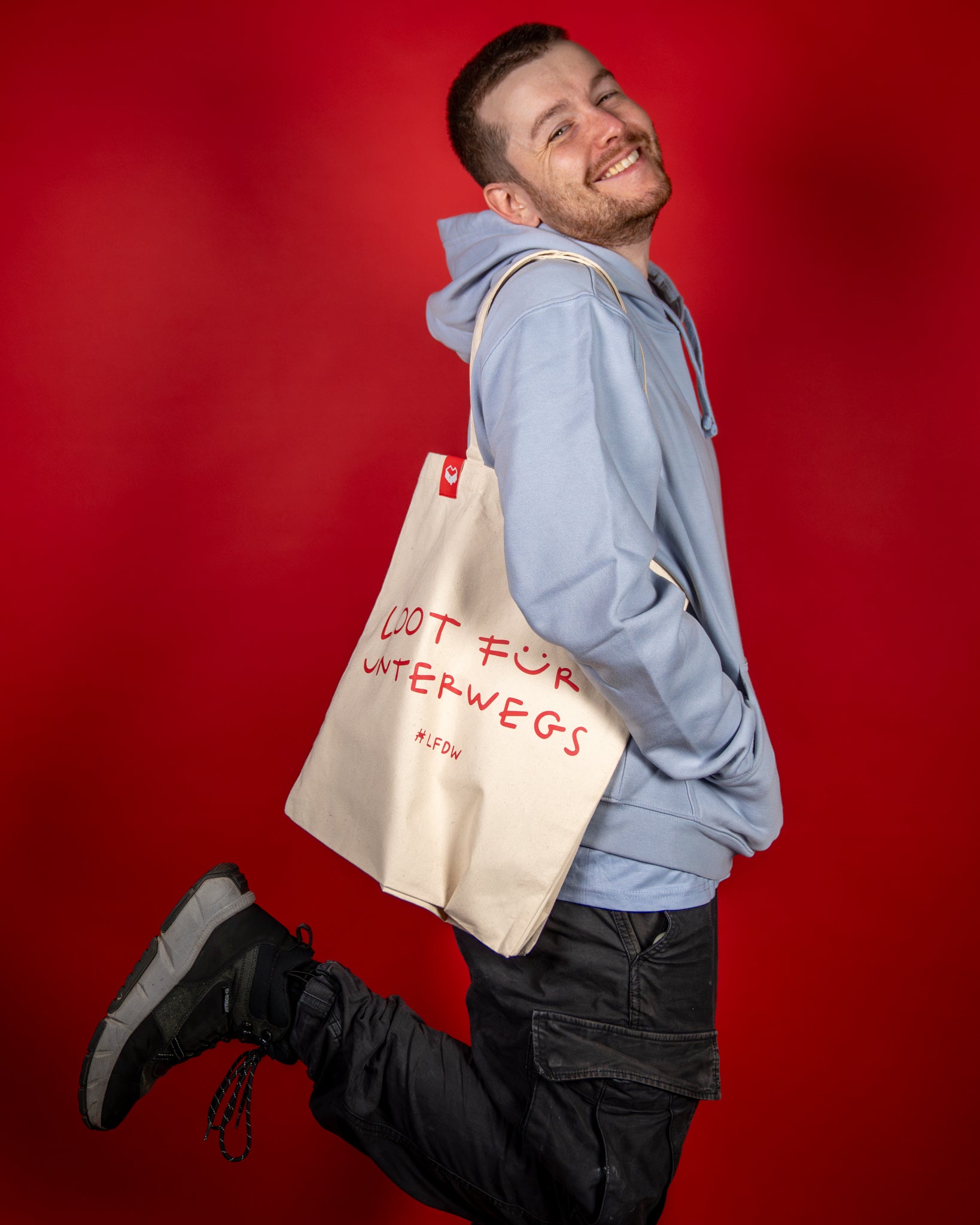 Hellblauer Hoodie aus weicher Baumwollmischung mit lockerer Passform und aufgesetzter Kängurutasche. Der Hoodie hat eine Kapuze mit Kordelzug und zeigt auf der Brust ein rundes Logo mit rotem Herzsymbol. Der Stoff wirkt glatt und bequem, ideal für Freizeit und Alltag.